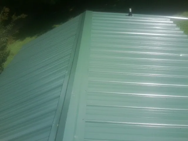 New green metal panels meeting at the ridge of a roof — Flat Roof Repair work by our crew in Syracuse