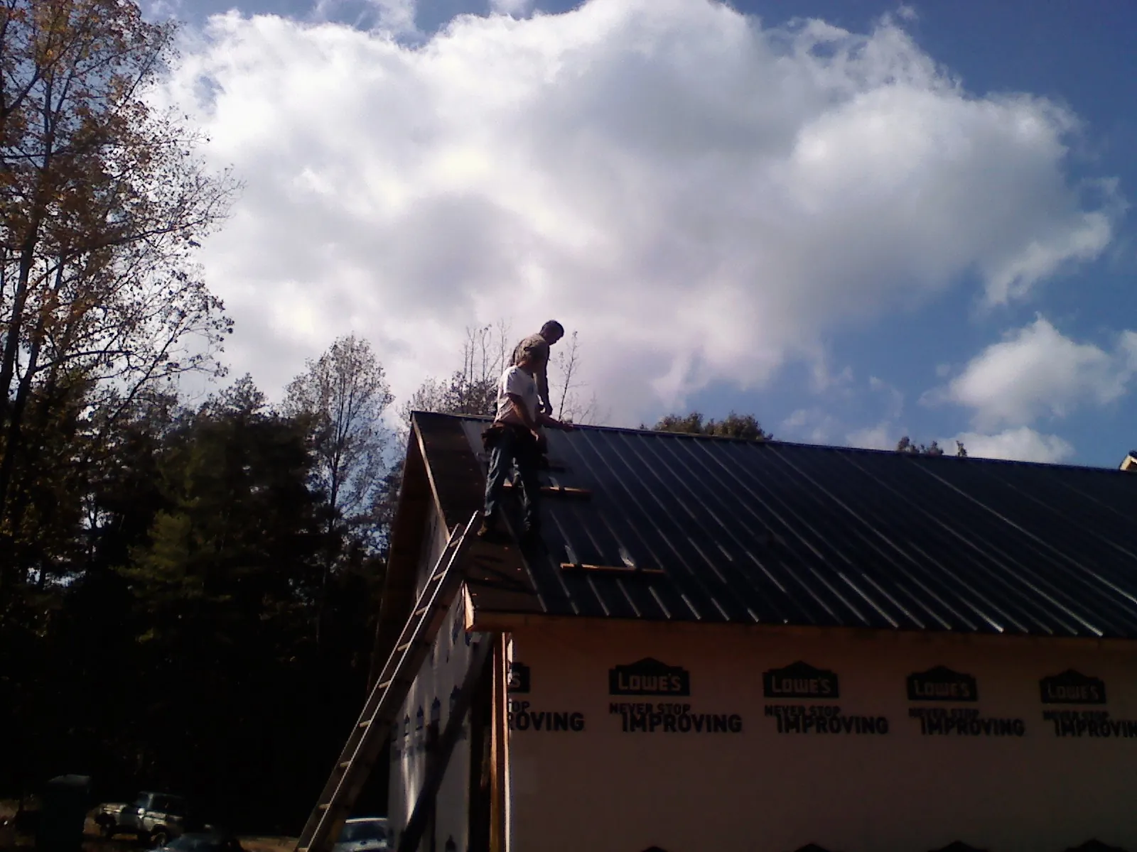 Roofer fastening dark metal panels high against a cloudy sky, from a Roof Inspection job in Syracuse